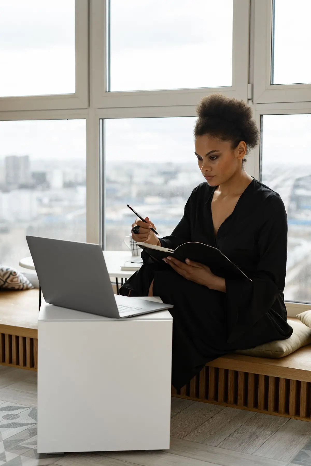Woman writing in a notebook with a laptop open beside her